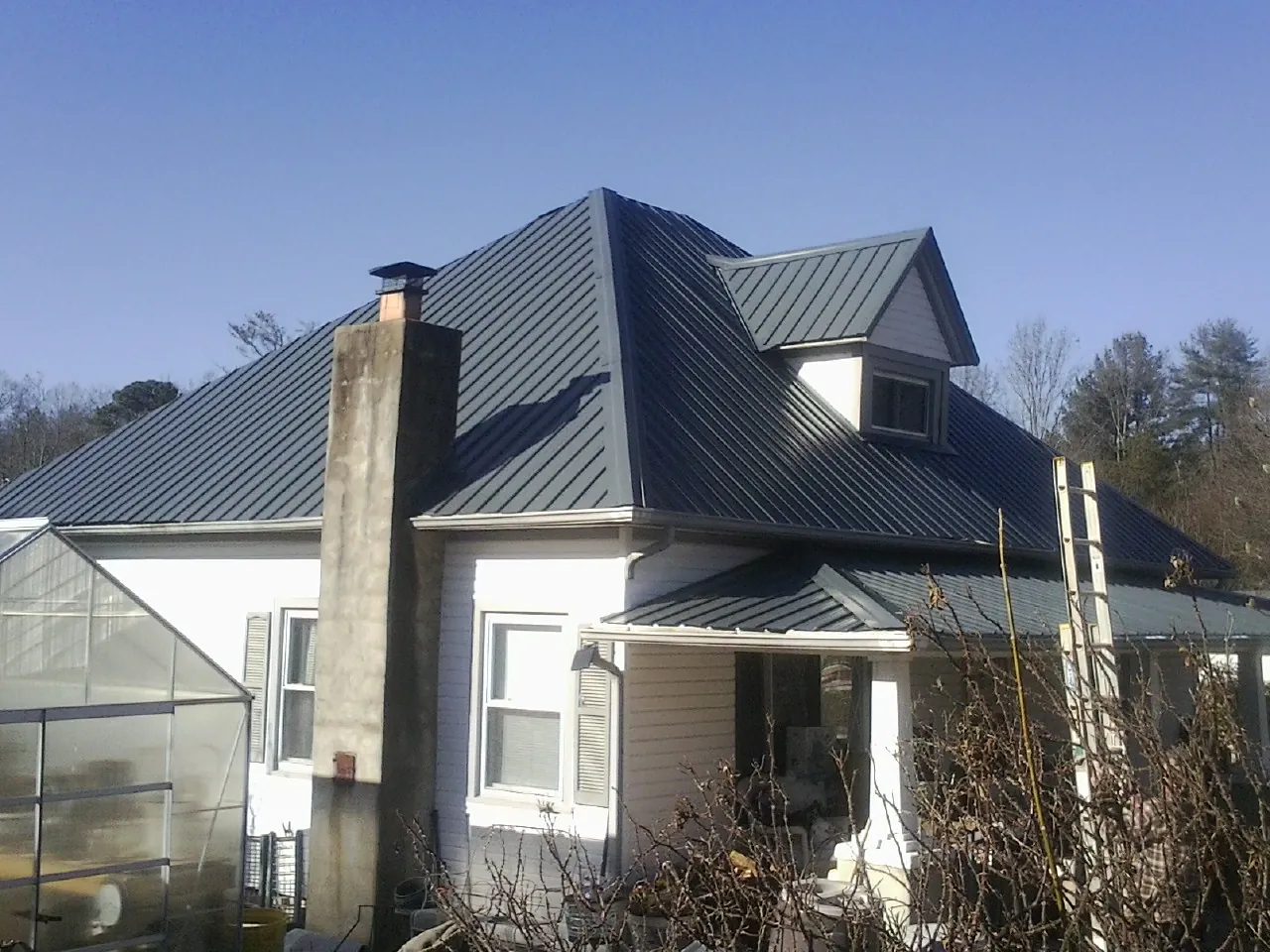 Dark blue standing seam metal roof on a white farmhouse with dormer — Slate & Tile Roof Repair by Roofing Brothers in Hanover Park