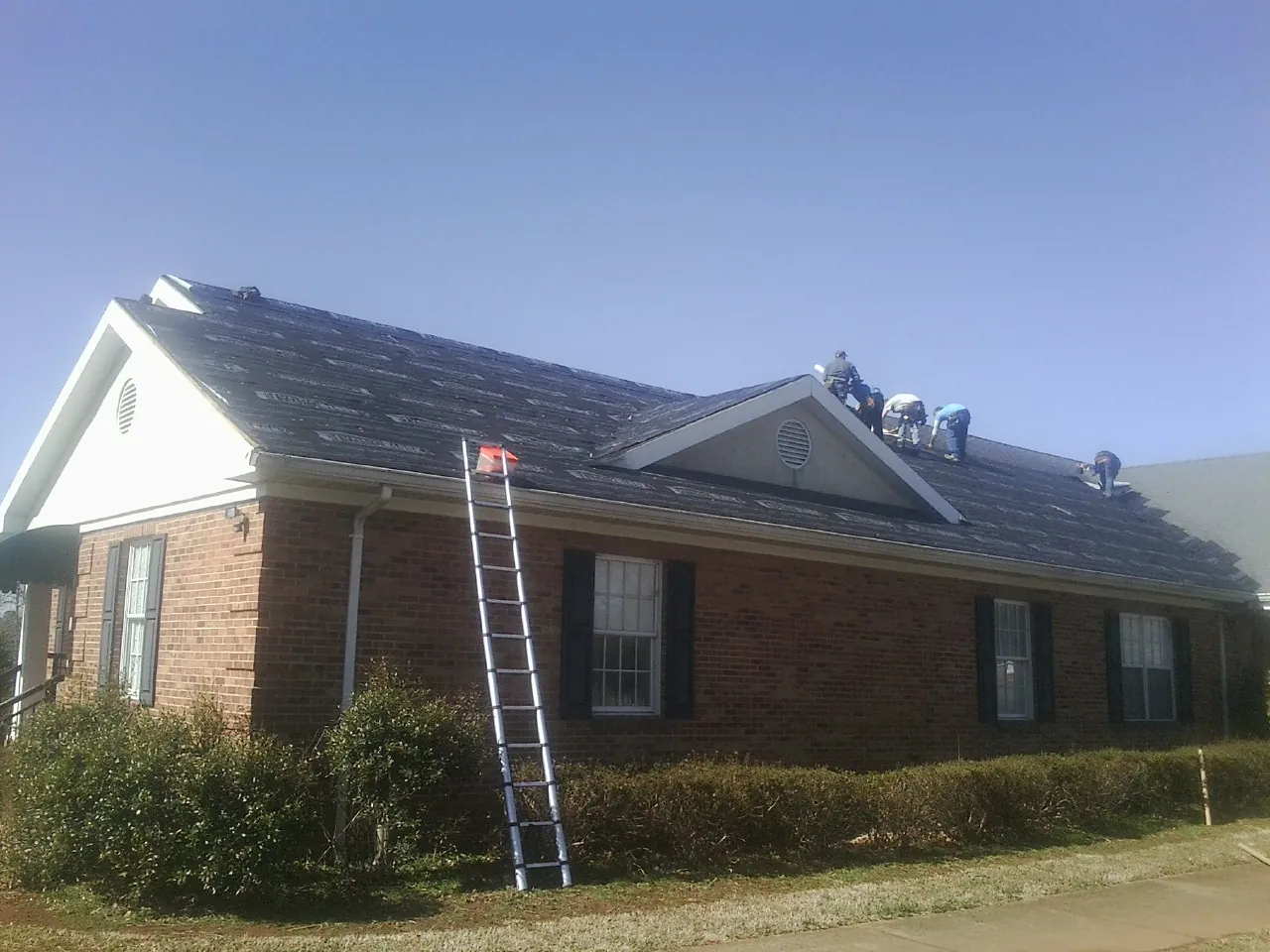 Crew tearing shingles off a brick ranch roof with a ladder set — Metal Roof Repair work by our crew in Hanover Park