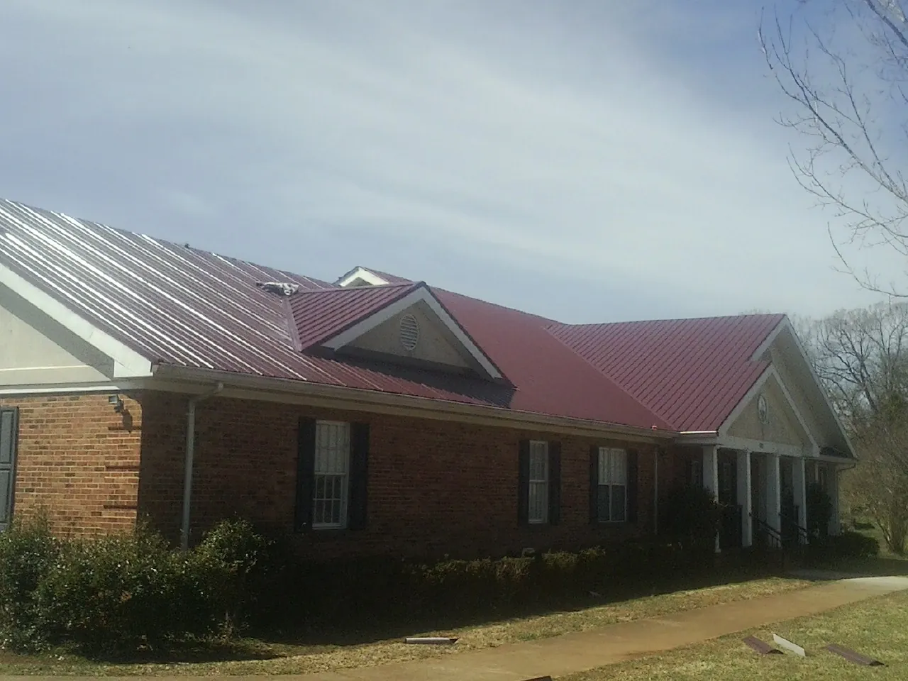 Red metal roof with gabled entries on a long brick building, from a Hail Damage Roof Repair job in Hanover Park