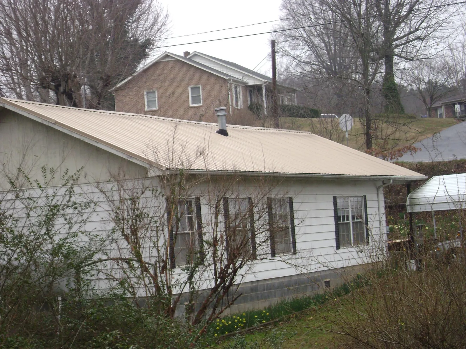Tan metal roof on a white sided house set into a hillside — Commercial Roofing by Roofing Brothers in Hanover Park